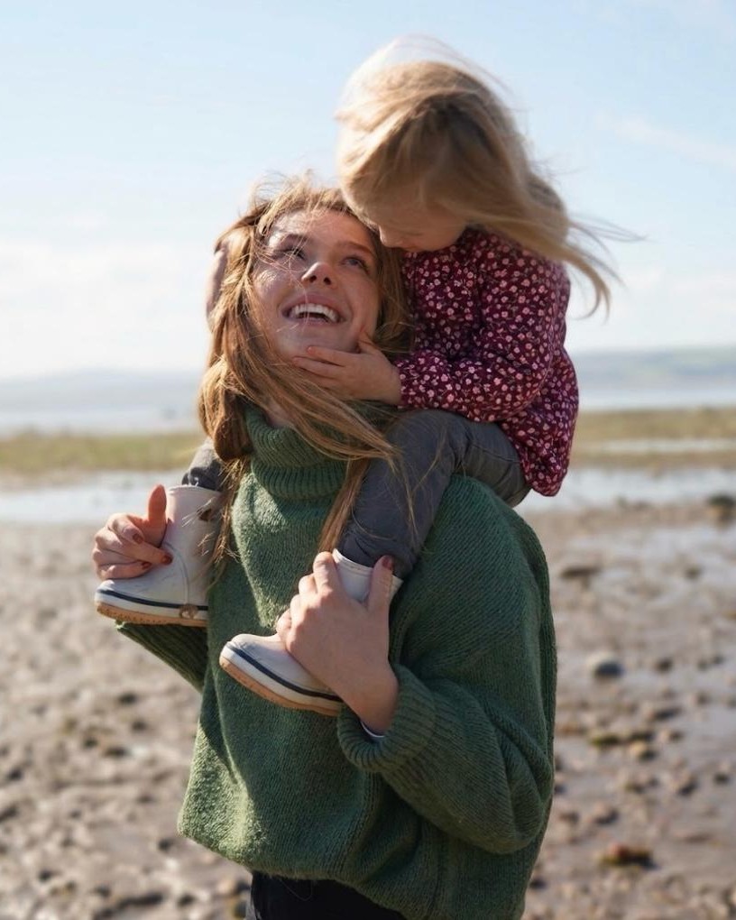 A mother carrying her daughter on her shoulders outdoors