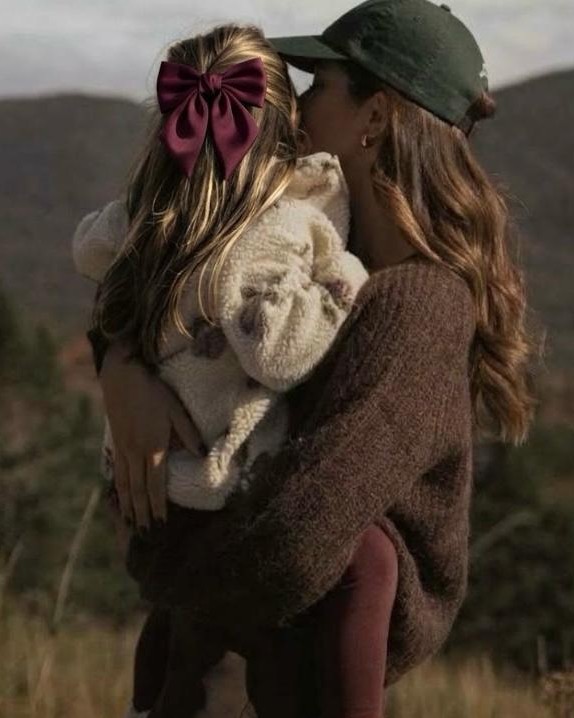 A mother holding her daughter outdoors, her face against the child&rsquo;s hair