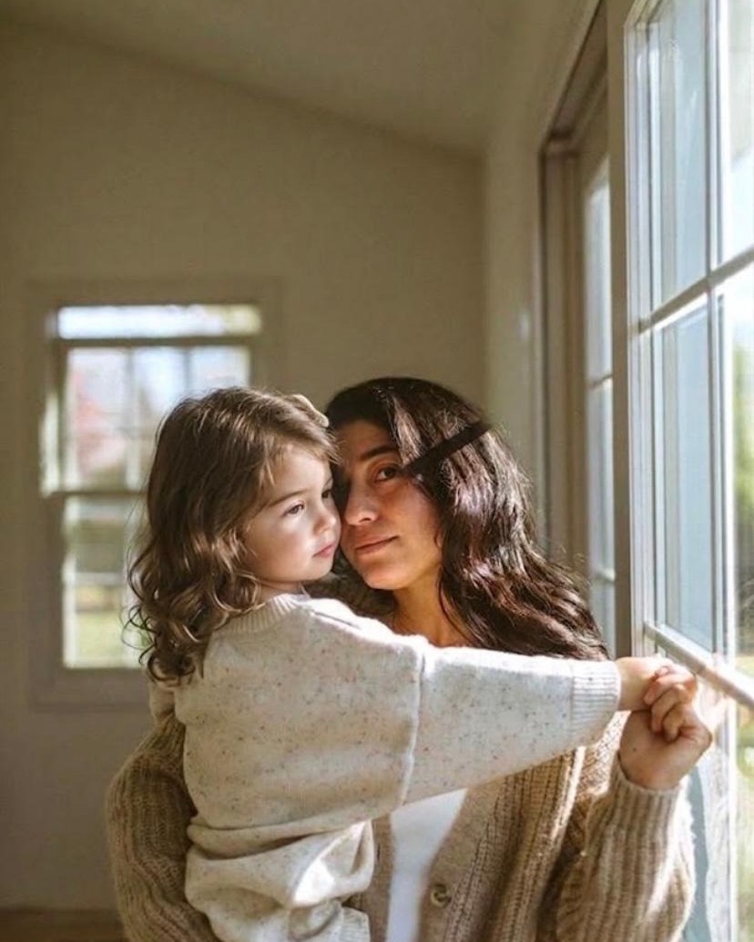 A mother holding her small daughter by a window in the afternoon light